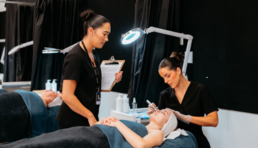 Beauty student with tutor applying a facial cream to client